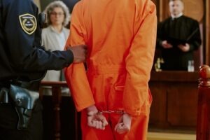 Defendant in an orange jumpsuit and handcuffs in a courtroom