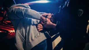 A police officer handcuffs someone and moves them toward a police car after charging them with resisting an unlawful arrest in Arizona.