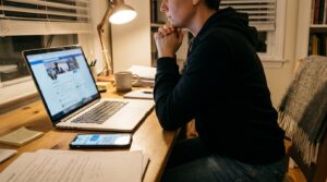 person at desk viewing social media profile on laptop with documents nearby