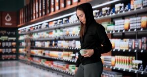 A woman stands in a store aisle holding an item. A lawyer can tell you what happens if you are arrested for shoplifting in Arizona.