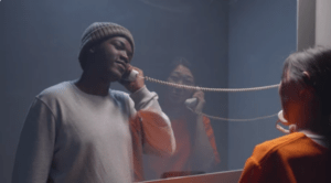 A man visiting his girlfriend in jail from behind glass.